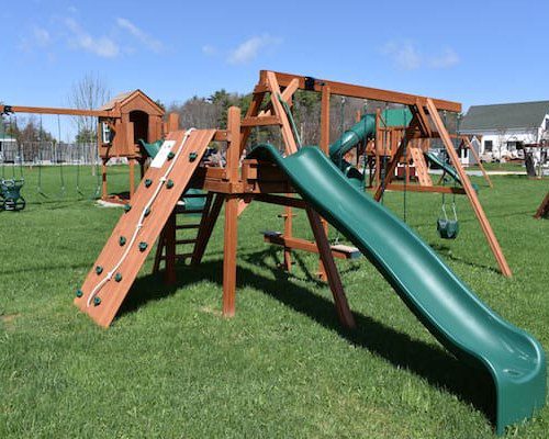 Backyard wooden play set with green slide and swings on grass