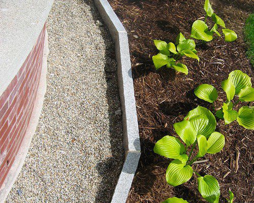 Stone-edged garden bed with hostas beside a gravel path